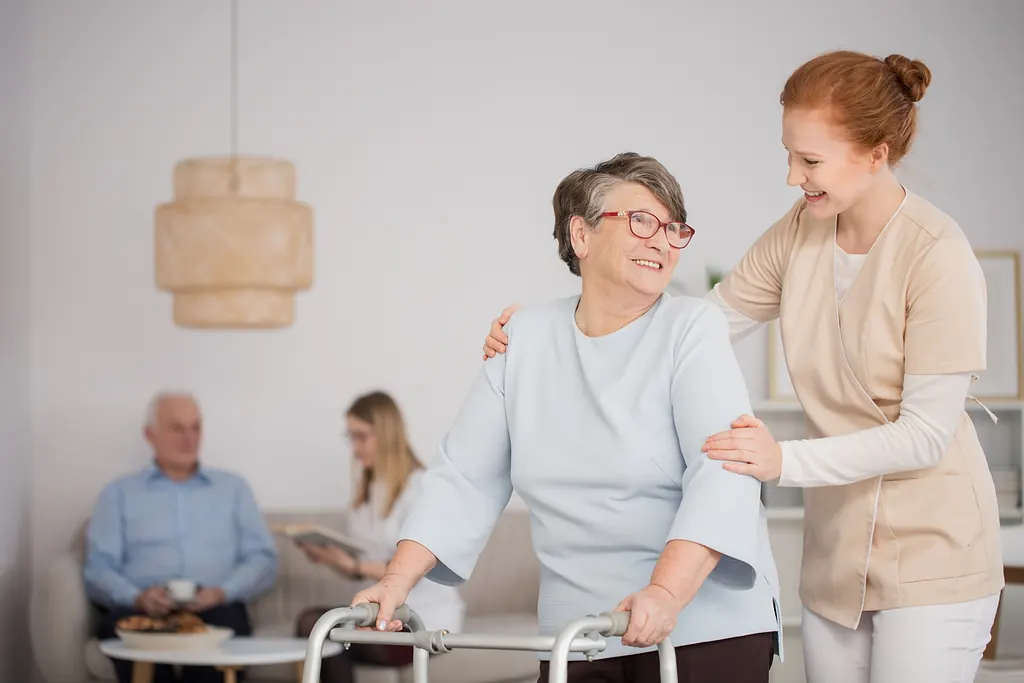 Pflegekraft begleitet eine ältere Dame mit Rollator