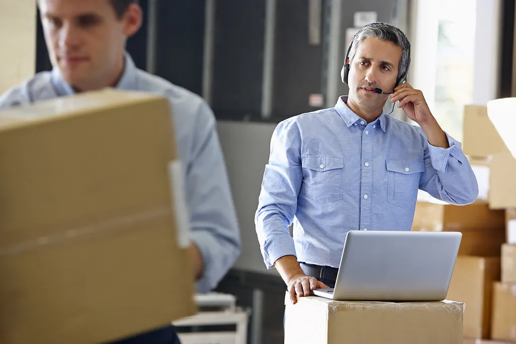 Mitarbeiter mit Headset und Paketen im Versandlager